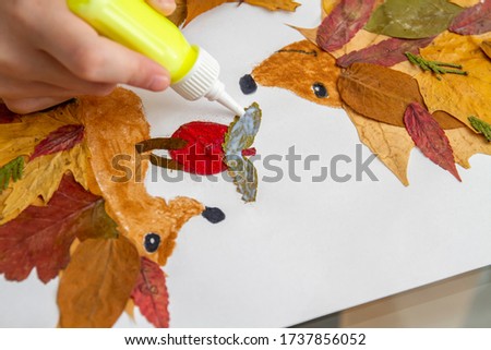 Girl makes an application from dry leaves. Children applique on the autumn theme. Hedgehogs and apple