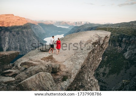 Young couple walking in troll tongue in norway in summer at sunset. Beautiful landscape, cliff, rocks, mountains. Royalty-Free Stock Photo #1737908786