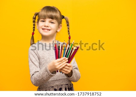 Portrait of happy lovely child girl drawing with colorful pencils isolated over yellow background