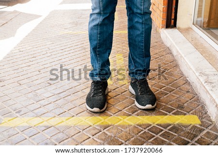 Maintain Social Distancing in yellow Waiting line attached in the ground. Prespective of a person's feet. Prevention concept