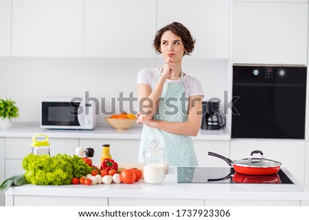 Photo of beautiful housewife holding arm on chin remind recipe minded enjoy weekend morning cooking tasty dinner family meeting wear apron t-shirt stand modern kitchen indoors Royalty-Free Stock Photo #1737923306