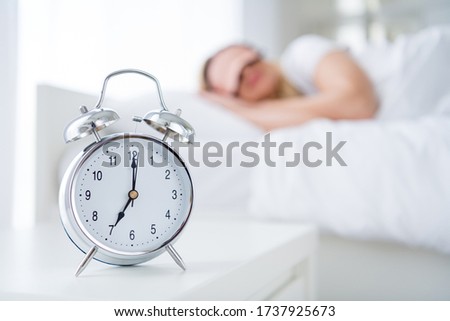 Profile photo of charming lady lying sleeping bed white sheets blanket clothes calm sure metal alarm clock will ring at sever o'clock morning work monday wear pajama room indoors
