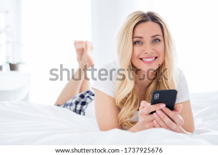 Closeup photo of cheerful beautiful house wife lady hold telephone writing blog post lying cosy bed freelancer quarantine white linen warm sunny morning stay home wear pajama room indoors