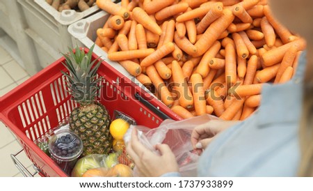 Woman chooses carrot in supermarket.
