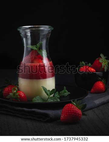 Italian food - Strawberry Panna Cotta with mint decoration in a glass in a dark setting