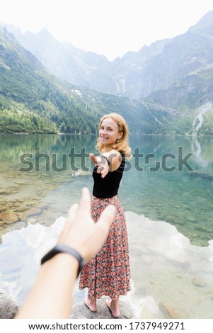 Follow me, first person view of traveler girl standing on stone edge in front of amazing lake and mountains, a girl holding the hand of her boyfriend