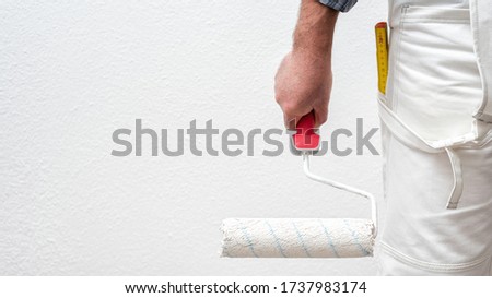 Caucasian house painter worker in white overalls, he holds the roller in his hand. Construction industry. Work safety.