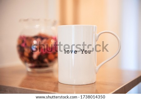 White ceramic mug inscribed with the words 'love you' on the front, sitting on wooden table with soft focus background