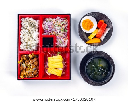 Top view of Japanese Bento Box with roll egg, mushroom with beef, salad and sauce. Seaweed soup and fruit. Bento set isolated on white background