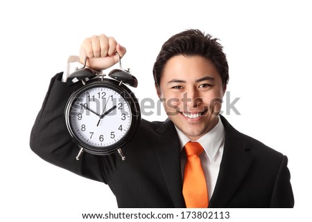 Attractive businessman holding a clock, wearing a suit and orange tie. White background.