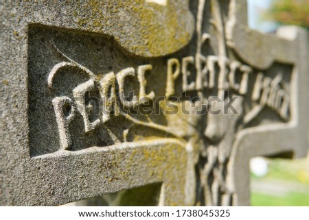 A gravestone shaped like a cross that says "peace perfect peace" at Wandsworth Cemetery in South West London. Image features shallow depth of field and has copy space.