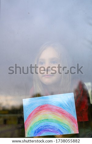 noisy effect. kid girl seven year old with drawing rainbow looks through the window during covid-19 quarantine. stay at home, let's all be well. vertical image