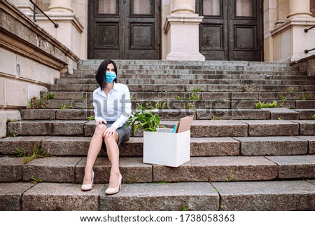 Young business woman in office siut sitting on old stairs with a box of her office supplies and sign looking for a job. Unemployment after corona virus.
