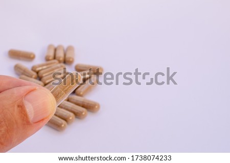 fingers holding herbal capsule, nutritional supplement, vitamin pill, herbal medicine on white background. Tribulus Terrestris