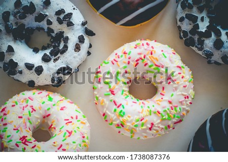 Flat lay image of donut with white glaze and colourful hundreds and thousands amids other different donuts
