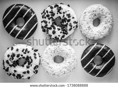 Flat lay image of six ring donuts with white glaze and hundreds and thousands, chocolate and stripes and white glaze with black cookies, black and white image 