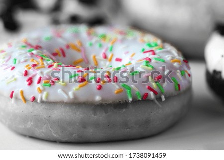 Close-up on ring donut with white glaze and colourful hundreds and thousands, black and white image with selected colour