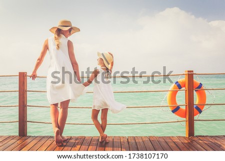 Suntanned woman and girl in white dresses enjoy sea view at the wooden pier. Vacation, get away, travel concept. Toned image