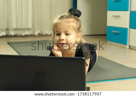 little girl in a gymnastics leotard lies on a gymnastic rug at home and is waiting for an online gymnastics lesson