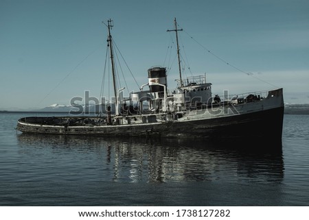 A view of an old sunken and abandoned ship in Ushuaia, the mountains can be seen in the distance. Monotone photography.