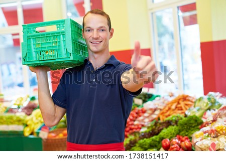 Smiling employee with vegetable crate in the supermarket holds his thumb up