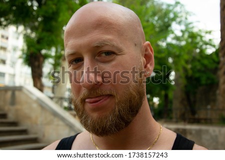 Handsome young European bearded hairless man is showing his tongue to camera. Stock image.