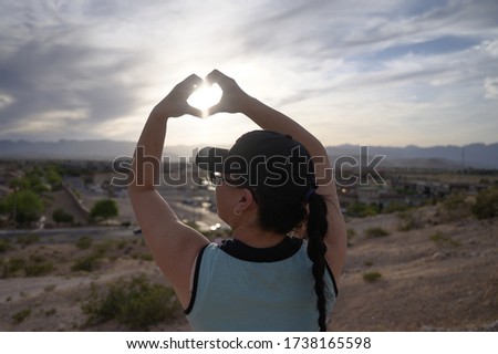 Woman making heart shapes with hand with sun in it.