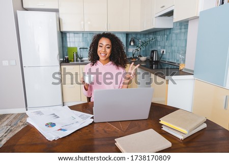 happy african american girl showing peace sign while holding cup and having video chat at home