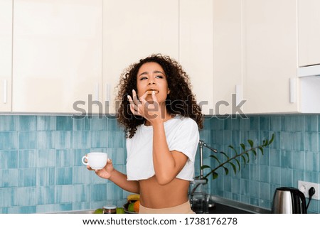 curly african american girl eating toast bread with jam and holding cup of coffee