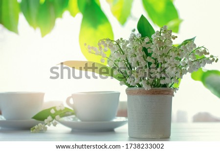 a bouquet of lilies of the valley and a cup of tea on the table close-up. morning tea and a bouquet of lilies of the valley.