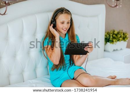 Pretty young teen girl in blue summer polo dress listening music at black ear-flaps and laptop on white background. Copy space