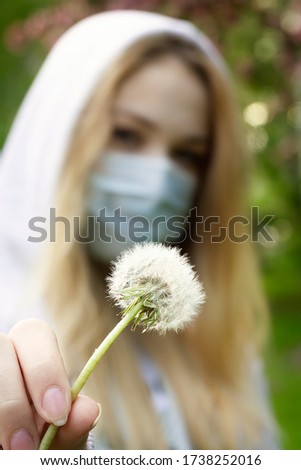 Dandelion is held by a European girl in a medical mask with light hair. corona virus concept. Life goes on concept. Life is wonderful.Make a wish