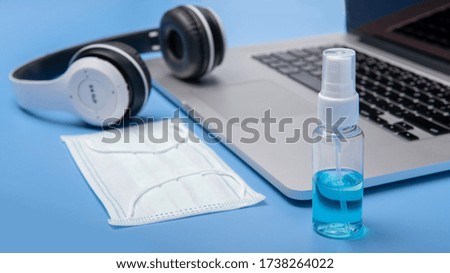 Stop the worldwide spread of сoronavirus COVID-19. The equipment work is currently at home on a blue background consisting alcohol spray. Mask, computer, headphones. Selective focus. Work from home