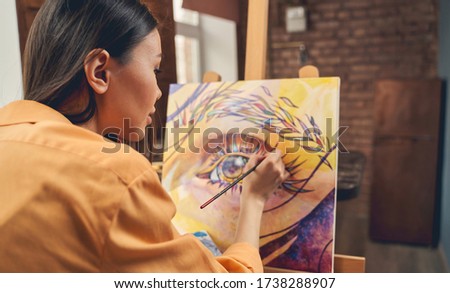 Charming brunette lady drawing beautiful picture with paints in home art studio