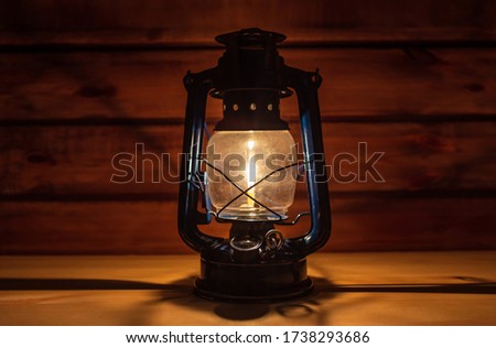 Vintage hand-held kerosene lamp illuminates with a soft glow in a dark room on the table. Vintage style. Light in the dark. Atmospheric photo in the loft style.
