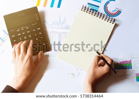 Photo of hands holding pen under document and pressing calculator buttons