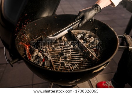 Close-up. Male cook in black gloves neatly transfers coals to the grill using tongs. Barbecue preparation