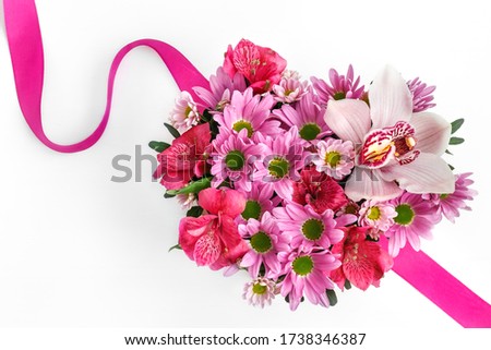 a beautiful heart-shaped box with flowers and pink ribbon on a white table, close-up with a blurry background. pink Orchid, chrysanthemum, Alstroemeria, as a birthday gift