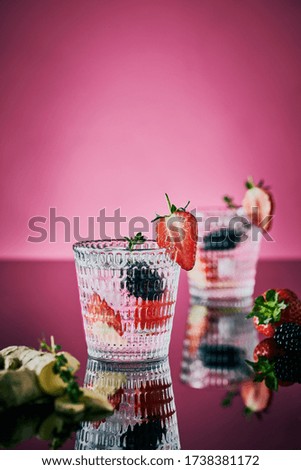 Textured glasses with gin and tonic decorated with slices of fresh berries on black reflective background