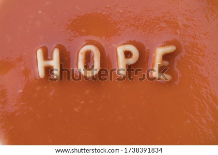 Orange pasta letters spelling the word "Hope" in red tomato sauce viewed from above