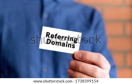 A man in a blue shirt holds a sign with the text of referring domain in one hand