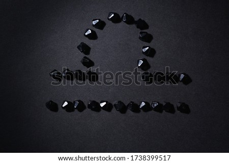 Symbol of the zodiac sign Libra made by black stones on a black background. Low dark key. Vignetting lighting. Horoscope Theme