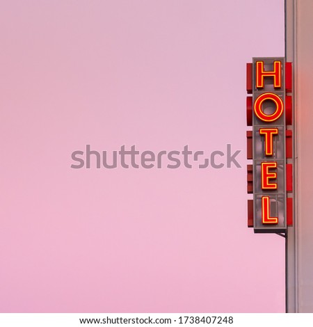 Neon hotel sign on the building corner with pink sunset sky at background. Empty copy space for inscription. Vintage neon sign.