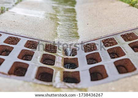 Closeup of rain water running down street gutter and flowing into storm sewer system drainage grate Royalty-Free Stock Photo #1738436267