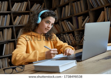 Hispanic teen girl, latin young woman school college student wear headphones learn watching online webinar webcast class looking at laptop elearning making notes or video calling remote teacher. Royalty-Free Stock Photo #1738498538