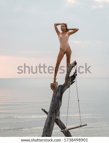 Fit slim caucasian woman on swing at beach at sunset time. Good shape female with long legs in trend swimsuit on tropical beach.