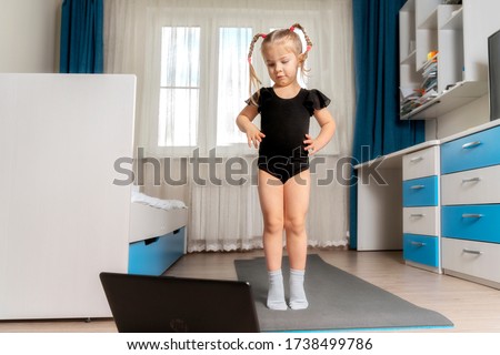 a child in a black giznastic bathing suit does yoga on a gymnastic rug at home in front of a computer. sports distance learning. space for text, copy space