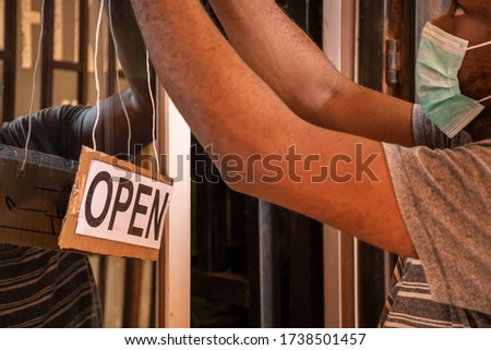 local african business owner putting up a open sign in front of his store