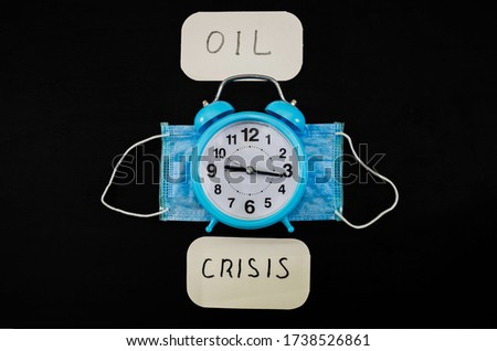 Phrase OIL Crisis and Disposable mask with clock on black background. Down of oil price, market decline. Financial world crisis concept. Coronavirus, 2019-nCoV.