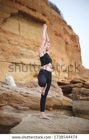 woman practices yoga by the sea on a cliff background.